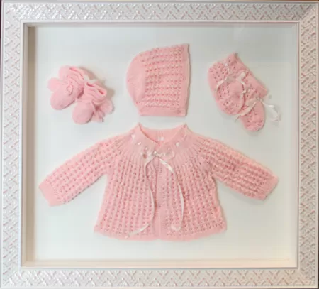 Baby clothing keepsake framing with a pink knitted sweater, bonnet, and booties in a shadowbox